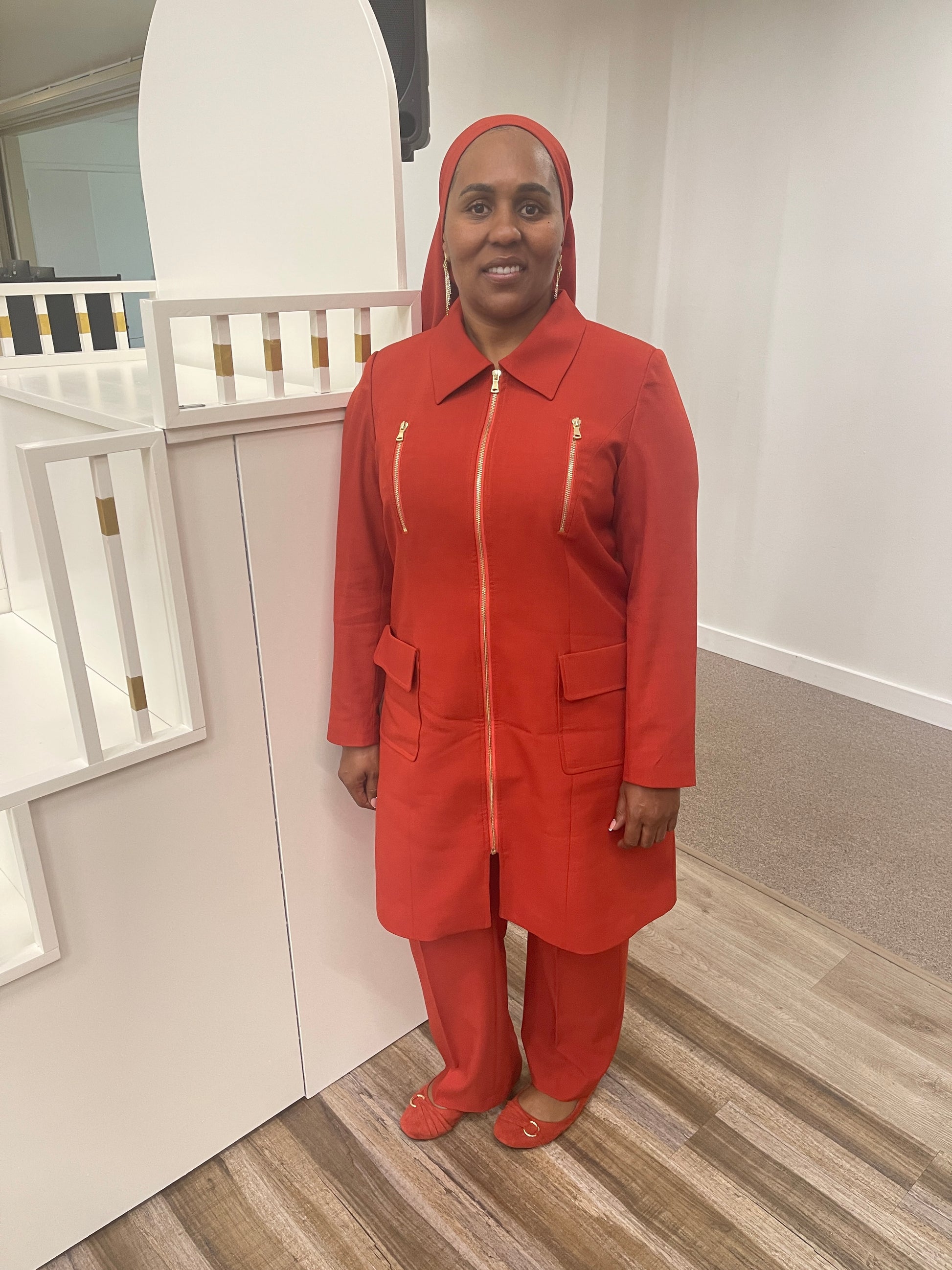 Full-body view of Vicky modeling the Rashidah three-piece red orange garment from a tilted front and side angle, designed for Muslim sisters in the Nation of Islam who value women's modest clothing.